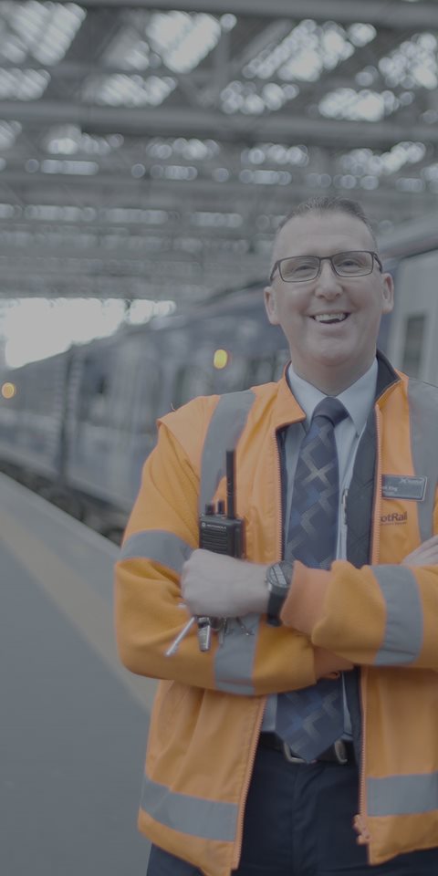 A close up shot of a rail employee smiling at the train station.