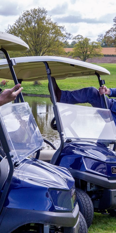 Two men standing on golf cars and smiling at the camera.